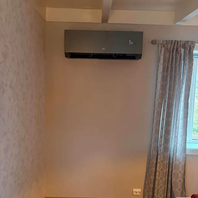 Innendørs varmepumpe i sort design fra Wilfa, montert over vindu i stuehjørne.